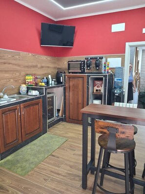 Cocina compacta con armarios de madera, microondas, cafetera y dispensador de agua.