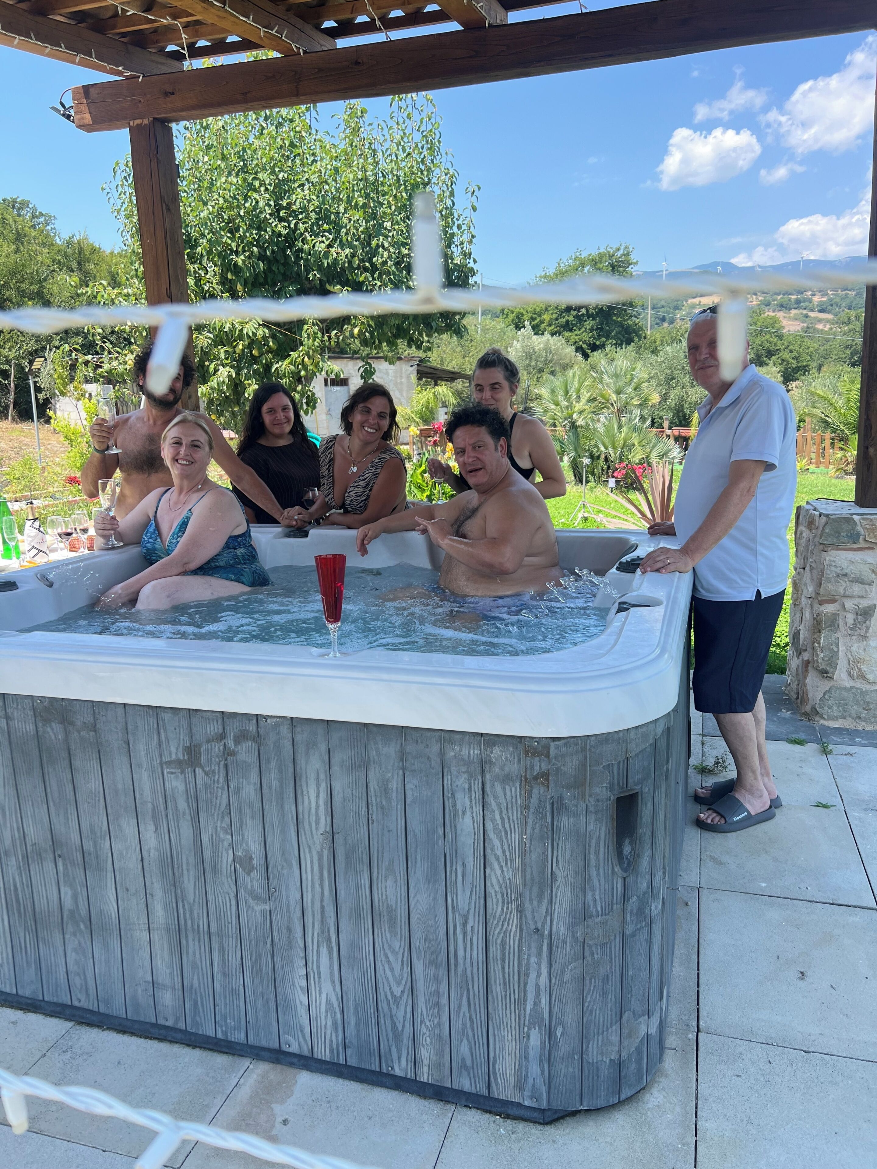 A group of people around a hot tub with a pergola overhead.