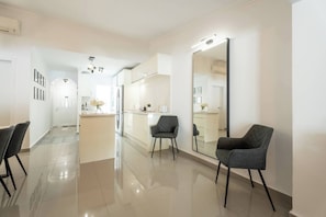 Une cuisine moderne dotée d’un grand îlot central, d’un coin repas avec des chaises et d’un couloir menant à une chambre.