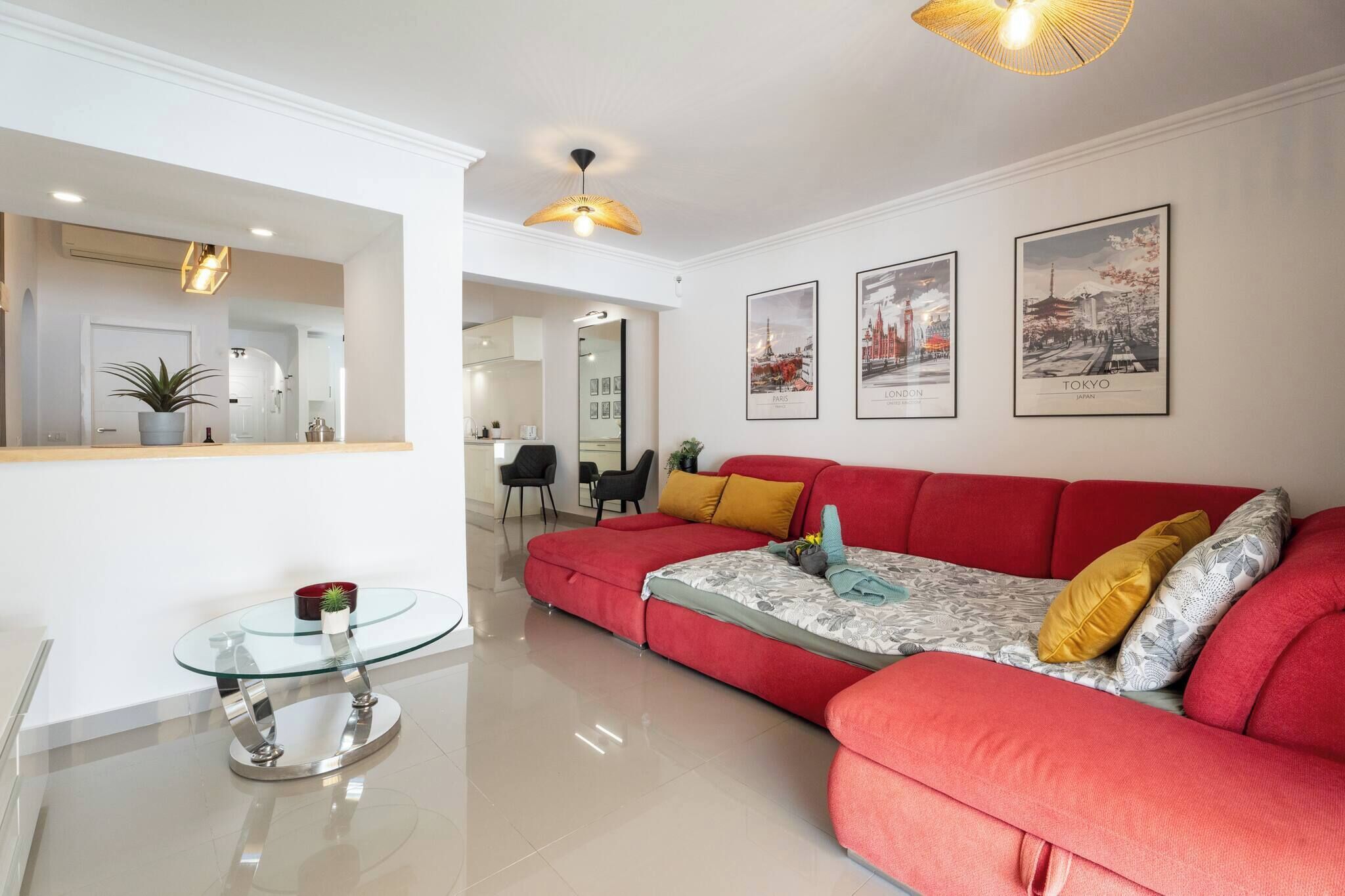 A modern living room with a red sofa, a glass coffee table, and framed cityscape pictures on the wall.