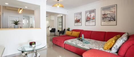 A modern living room with a red sofa, a glass coffee table, and framed cityscape pictures on the wall.
