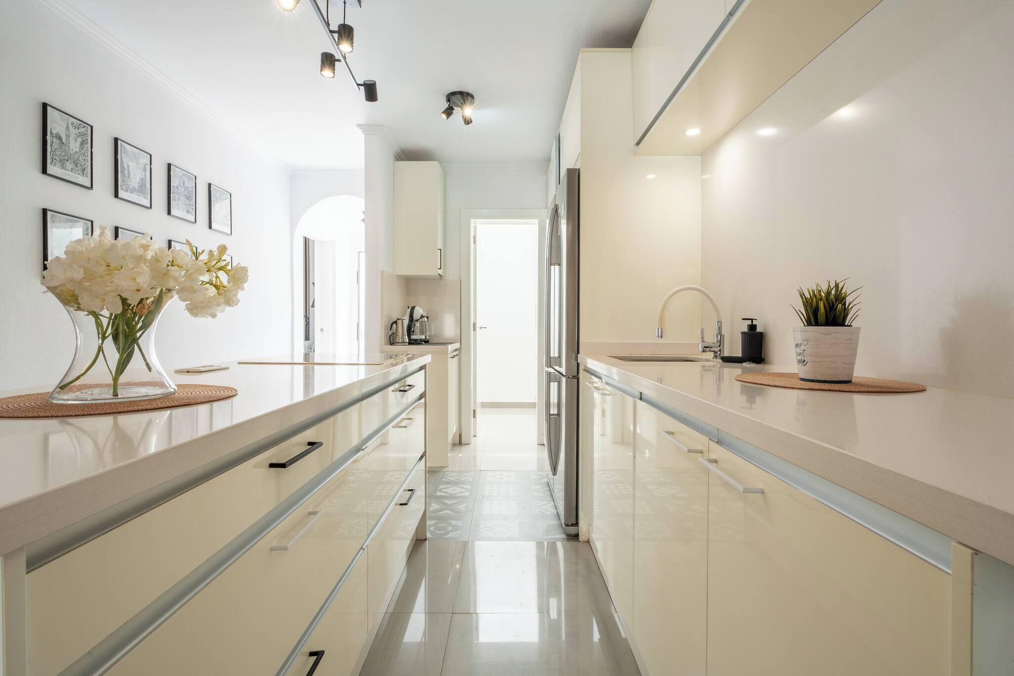Une cuisine moderne avec des meubles blancs, un îlot central et un vase rempli de fleurs blanches.