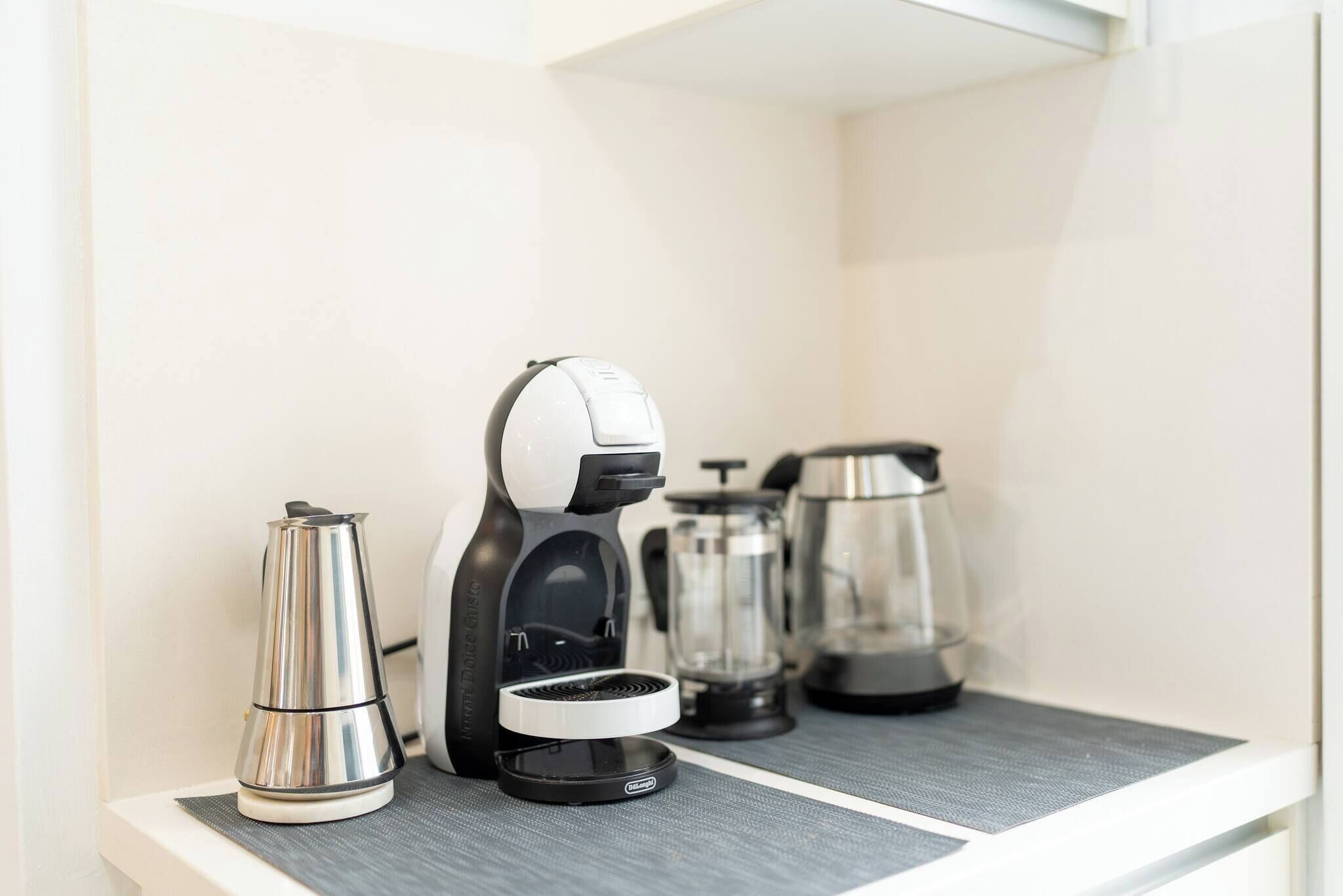 A kitchenette with a coffee maker, a kettle, and a French press.