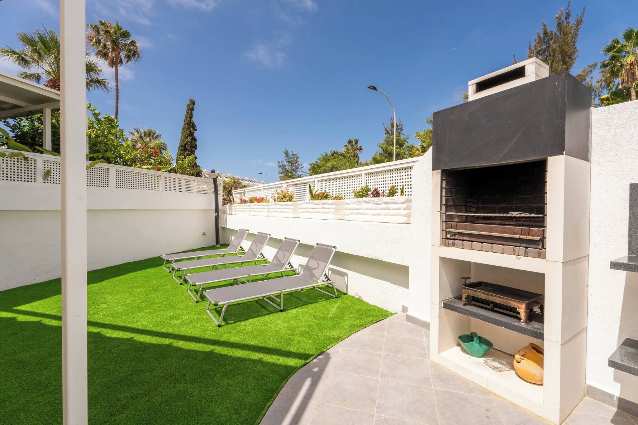 Eine Terrasse mit Kunstgr Rasen, Liegest ühlen, einem Grill und einem weißen Zaun.