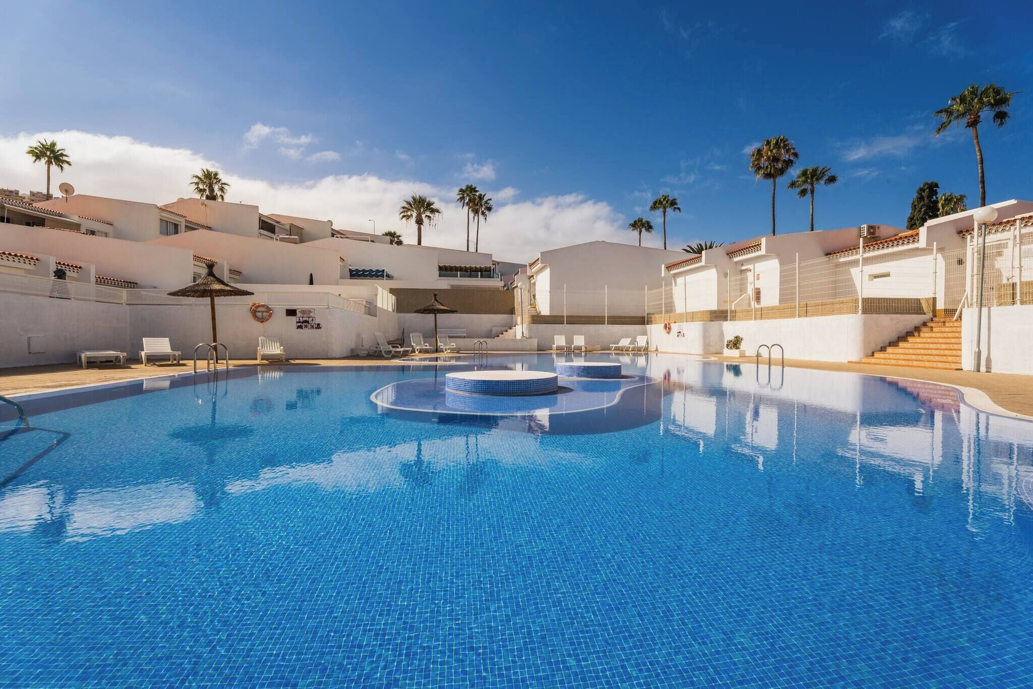 A swimming pool with lounge chairs, palm trees, and a clear sky.