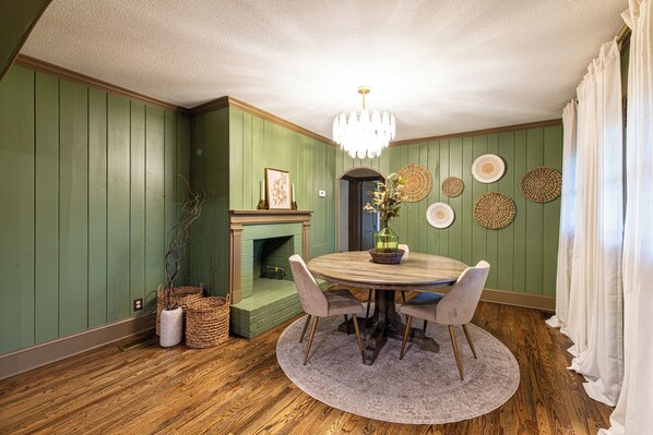 A dining room with a round table, chairs, a chandelier, a fireplace, and decorative wall plates.