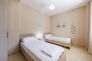 Ein Schlafzimmer mit zwei Einzelbetten, einem Nachttisch mit Lampe, einem Wandregal mit Dekorationen und einem Gemälde von Segelbooten.