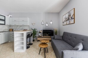 Eine moderne Küche mit weißen Schränken, ein Essbereich mit grauem Sofa, einem Fernseher und Wandkunst.