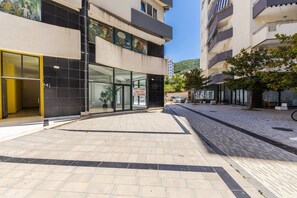 Un bâtiment avec une entrée en verre, une cour dallée et une voiture garée.
