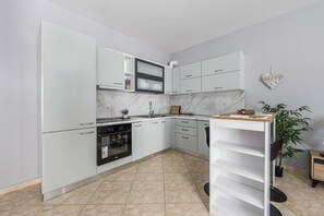 Une cuisine moderne avec des meubles blancs, un four encastré, un pare-feu en marbre et un petit coin repas agrémenté d’une plante.