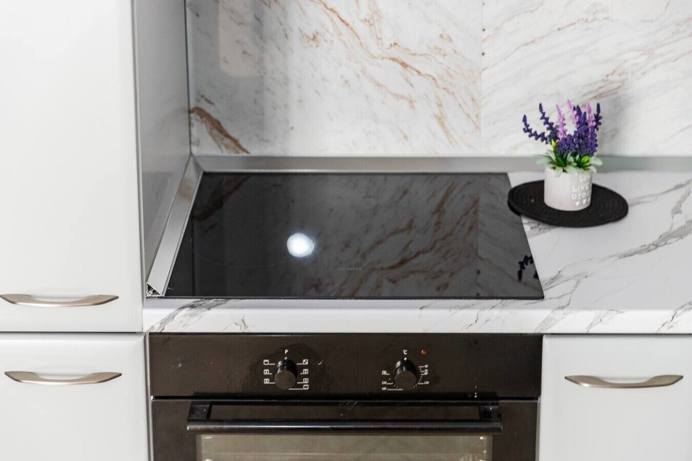 A kitchen with a black induction cooktop, a built-in oven, and a marble backsplash.