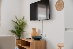Uma sala de estar moderna com uma TV de tela plana na parede, uma mesinha de madeira com uma tigela e um vaso, uma planta em vaso e um enfeite de palha na parede.