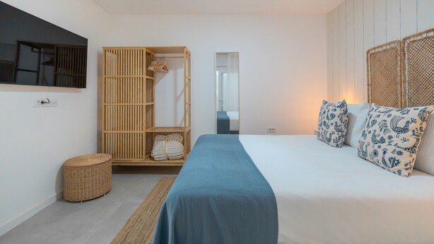 Une chambre à coucher comprenant un lit, une armoire, un miroir et un petit panier rond en osier.