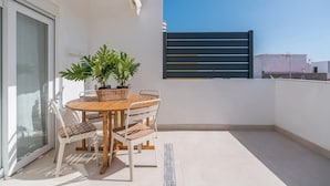 Un balcon avec une table et des chaises, un pot de fleurs et une vue sur le ciel.