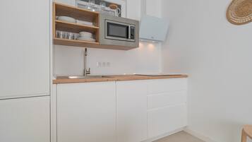 Une cuisine avec des meubles blancs, un plan de travail en bois, un four à micro-ondes et une étagère murale où sont rangés de la vaisselle.
