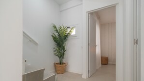 Een gang met een kamerplant, een raam en een deur naar een andere kamer.