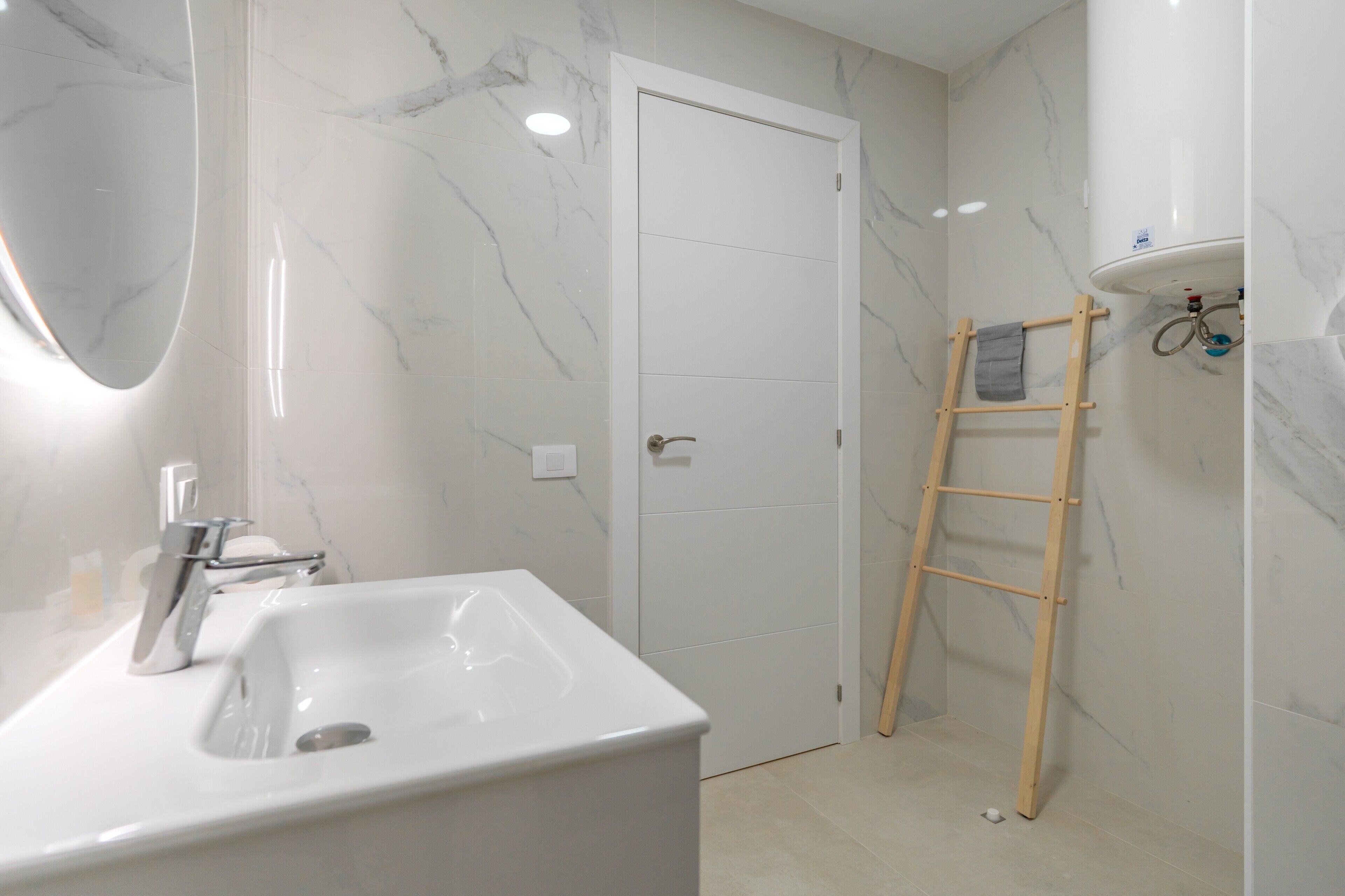 Une salle de bain avec un lavabo blanc, un miroir et des murs en marbre.