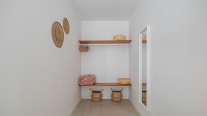 Een gang met een witte muur, een houten plank met manden, en een deur naar een andere kamer.