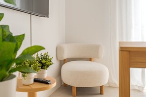 Ein modernes Wohnzimmer im minimalistischen Stil mit einem weißen Sessel, einem Holztisch mit Fernbedienung und Topfpflanzen.