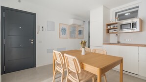 Een moderne keuken met een ingebouwde magnetron, een eettafel met rieten stoelen, en een donkere deur.