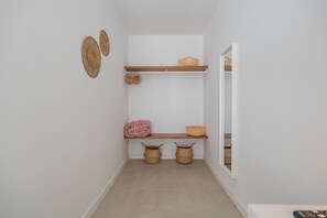 Ein Flur mit weißer Wand, einem Holzregal mit Körben und einer Tür zu einem anderen Raum.