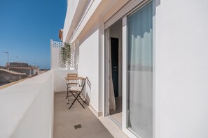 Ein Balkon mit Tisch und Stühlen, eine Schiebetür und Blick auf die Stadtlandschaft.