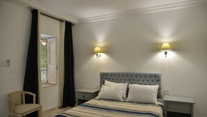 Ein Schlafzimmer mit einem Bett, zwei Nachttischen, einem Sessel und einem Fenster mit Vorhängen.