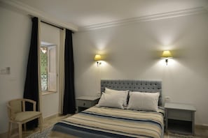 Un dormitorio con una cama, dos mesitas de noche, una silla y una ventana con cortinas.