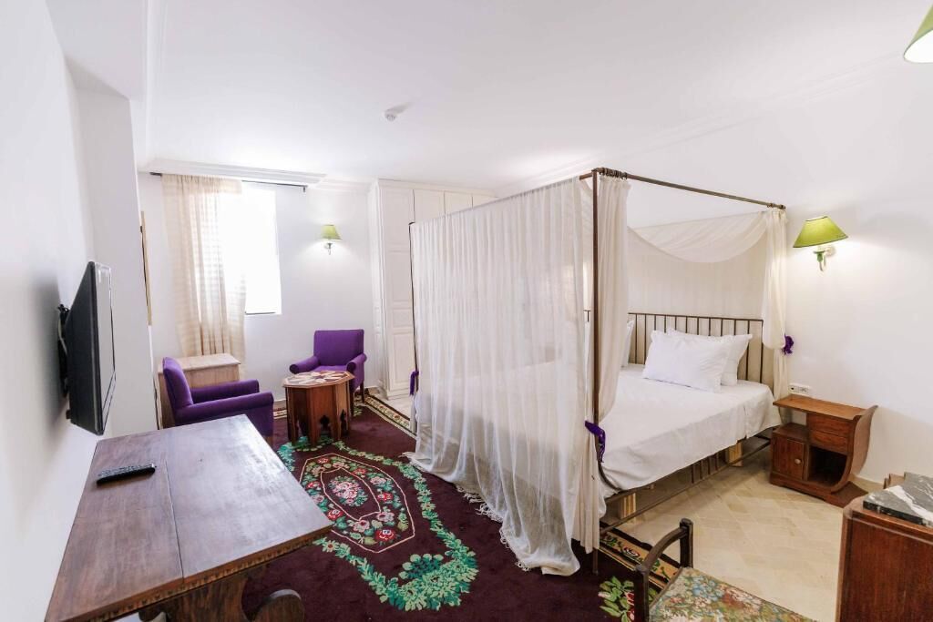 A bedroom with a four-poster bed, a TV, a desk, and a chair.