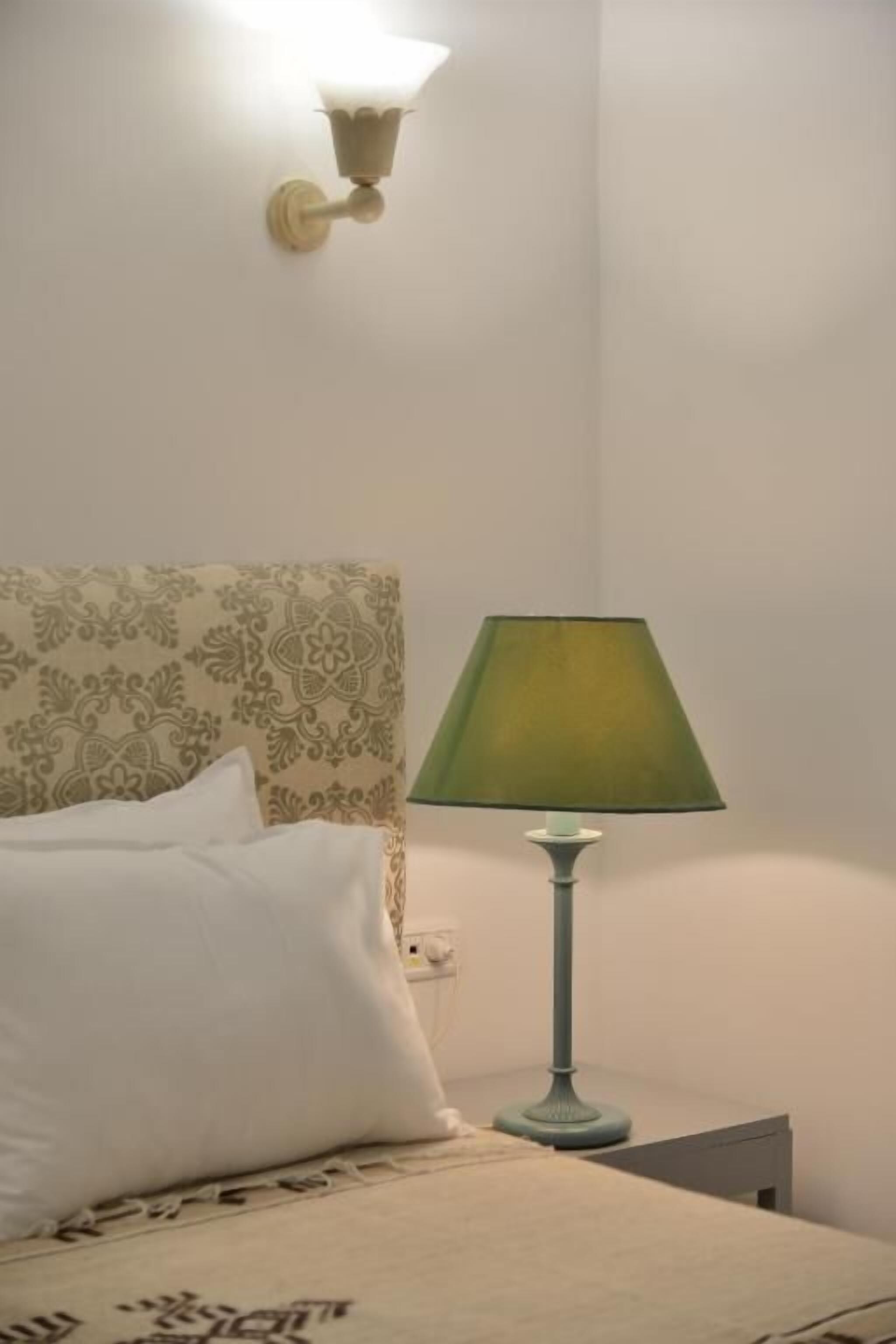 Una cama con un cabecero estampado, una lámpara de mesa verde y un aplique de pared.