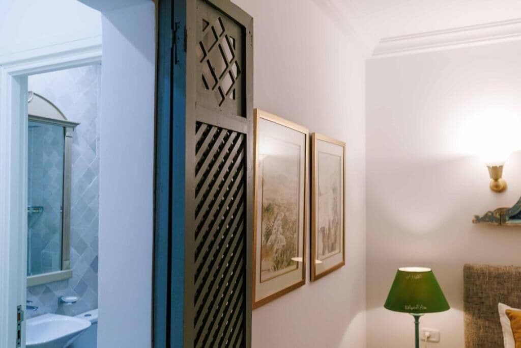 A bathroom with a shower, a sink, and a toilet. There are framed pictures on the wall and a green floor lamp.