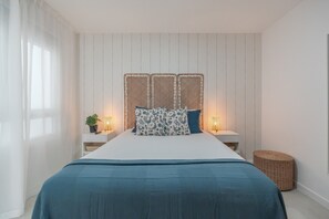 Een slaapkamer met een bed, nachtkastjes, een lamp, een plant en een rieten mand.