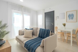 A modern living room with a sofa, a dining table with chairs, a door, and a framed picture on the wall. - Vacation Apartment 'Isabel 4' with Balcony, Wi-Fi and Air Conditioning (Guargacho)