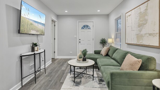 A living room with a sectional sofa, a coffee table, a TV mounted on the wall, and a door with a window.