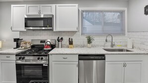 A modern kitchen with white cabinetry, stainless steel appliances, and a window with blinds.