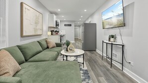 A modern living room with a sectional sofa, a coffee table, a flat-screen TV, and a kitchen area in the background.