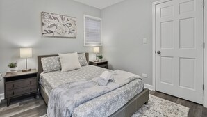 A bedroom with a bed, nightstands, a door, and a wall-mounted artwork.