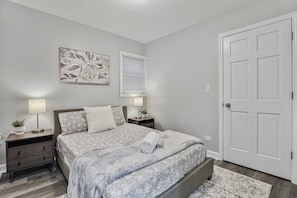 A bedroom with a bed, nightstands, a door, and a wall-mounted artwork.