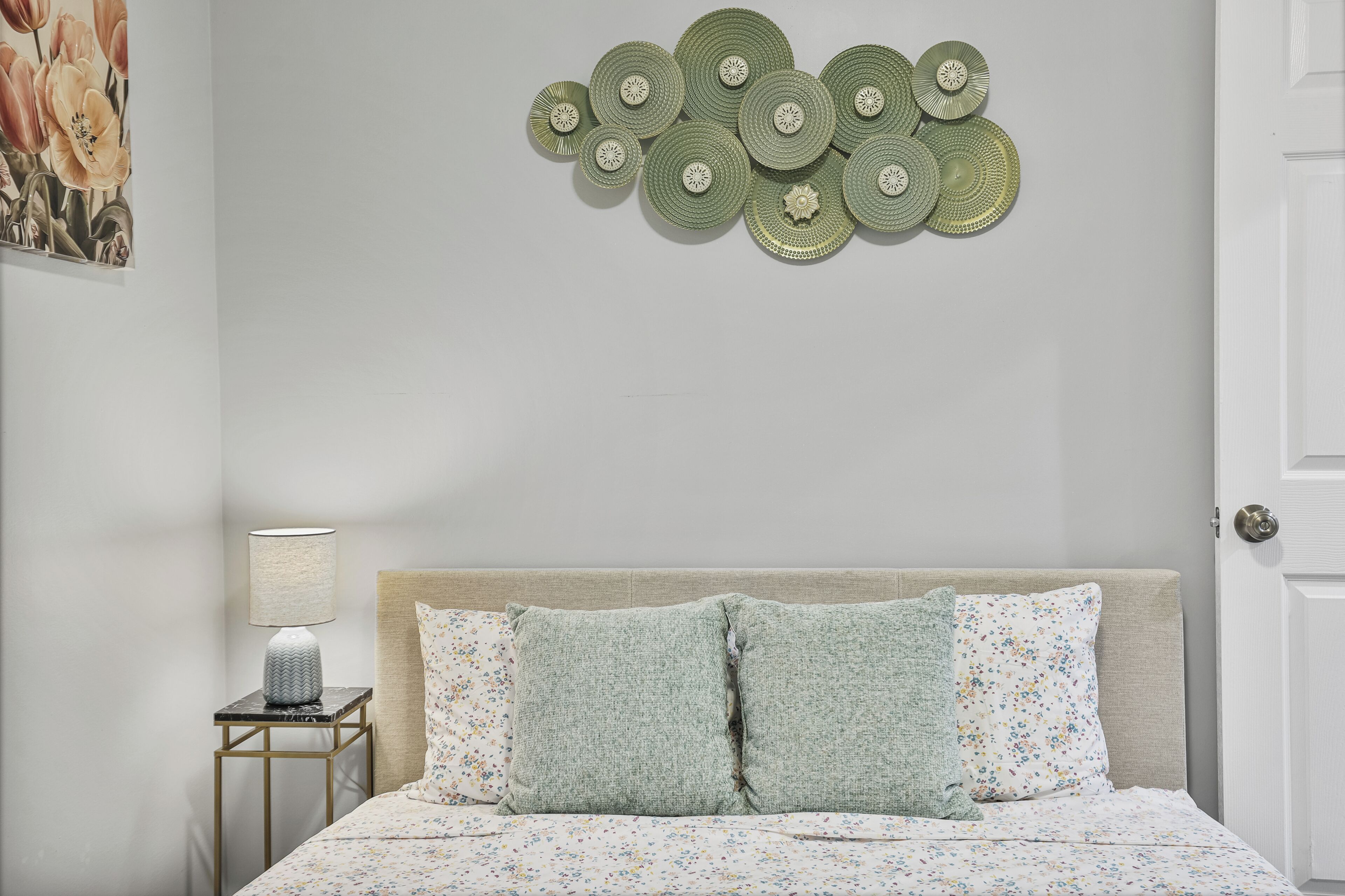 A bedroom with a bed, pillows, a nightstand, a lamp, and wall decor.