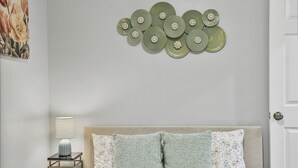 A bedroom with a bed, pillows, a nightstand, a lamp, and wall decor.