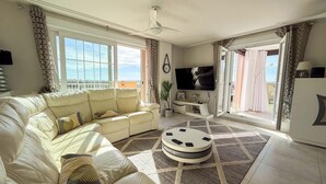 A living room with a sofa, a coffee table, a TV, and a balcony with curtains. - Spacious Penthouse • Large Sun Terraces • HYA01 (Isla Canela)