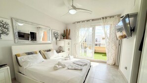 A bedroom with a bed, bedside tables, a TV, a ceiling fan, and a window with curtains. - Spacious Penthouse • Large Sun Terraces • HYA01 (Isla Canela)
