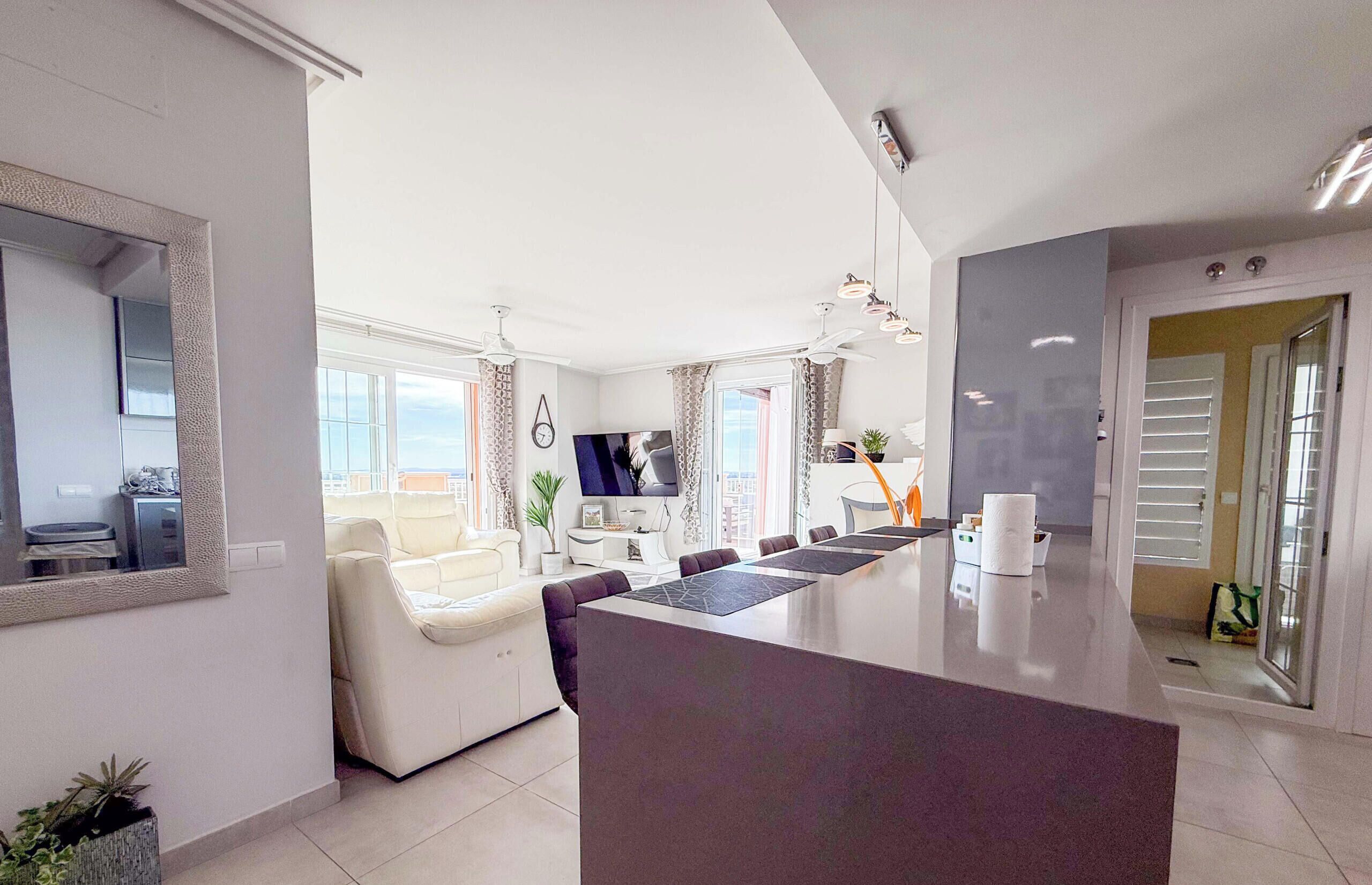 Eine moderne Küche mit Kochinsel, ein Essbereich mit Stühlen und ein Wohnzimmer mit Sofa und Fernseher.