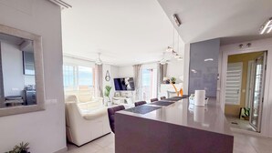 A modern kitchen with a central island, a dining area with chairs, and a living room with a sofa and TV. - Spacious Penthouse • Large Sun Terraces • HYA01 (Isla Canela)