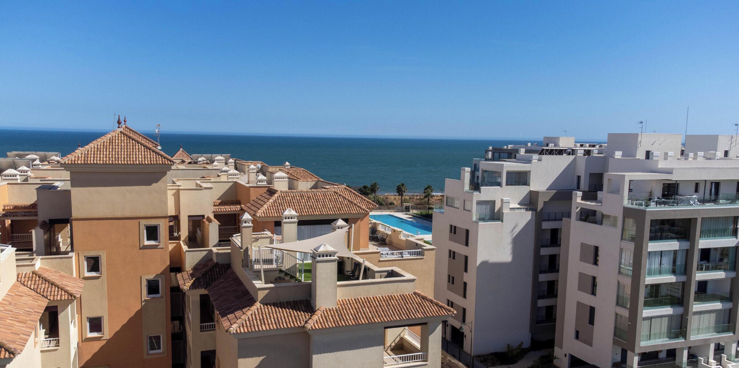 A coastal hotel with multiple buildings, a rooftop pool, and a view of the sea.