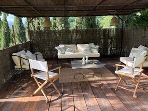 An outdoor seating area with a wooden deck, a cushioned sofa, two armchairs, and hanging lanterns. - Villa with Saltwater Pool, Private Garden, and Park in Mugello (Barberino di Mugello)