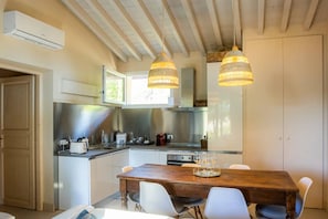 A modern kitchen with a wooden dining table, white chairs, and two hanging light fixtures. - Villa with Saltwater Pool, Private Garden, and Park in Mugello (Barberino di Mugello)