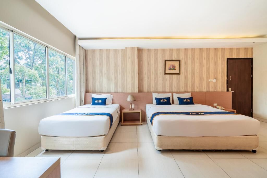 A hotel room with two beds, a desk, and a window with a view of trees.