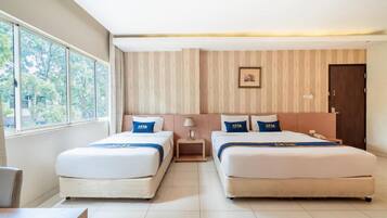A hotel room with two beds, a desk, and a window with a view of trees.