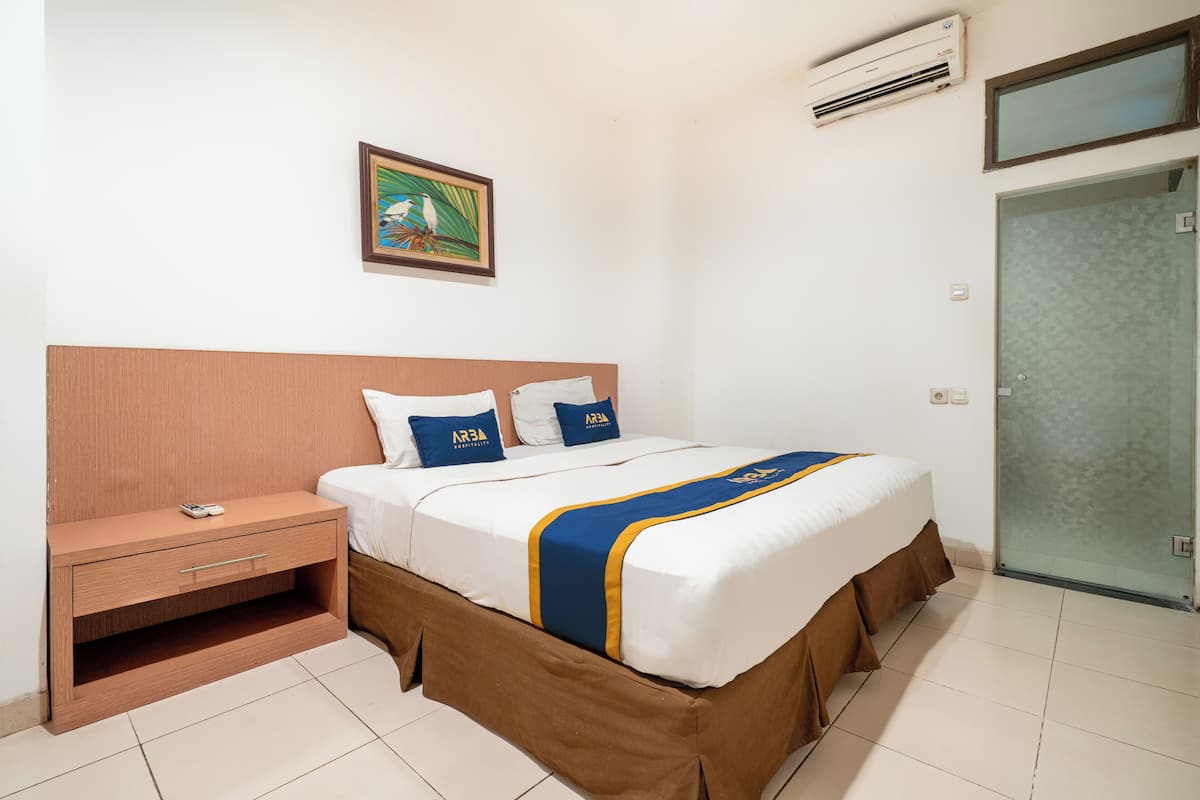 Ein Hotelzimmer mit einem Bett, einem Nachttisch, einer Wand-Klimaanlage, einem gerahmten Bild und einer Schiebetür.